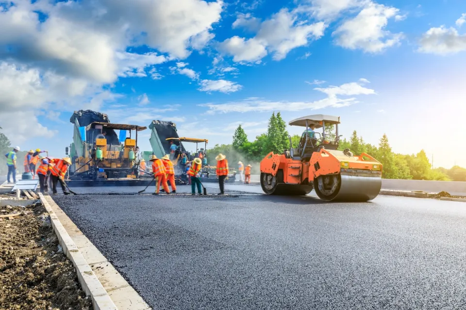 Orange and black heavy equipment and workers building new asphalt roadway.